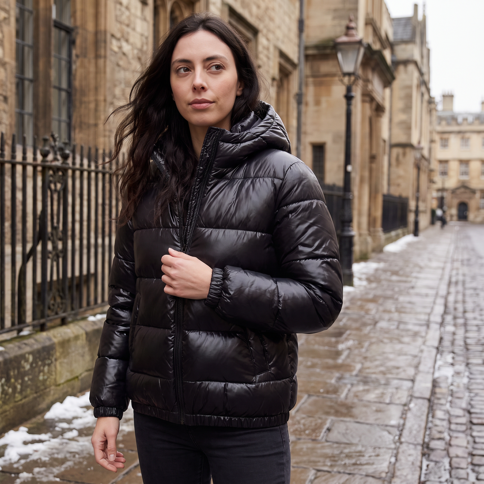 Women's black puffer jacket featuring a stylish attached hood, glossy quilted design, and convenient zip pockets, designed for a relaxed fit perfect for winter wear 3