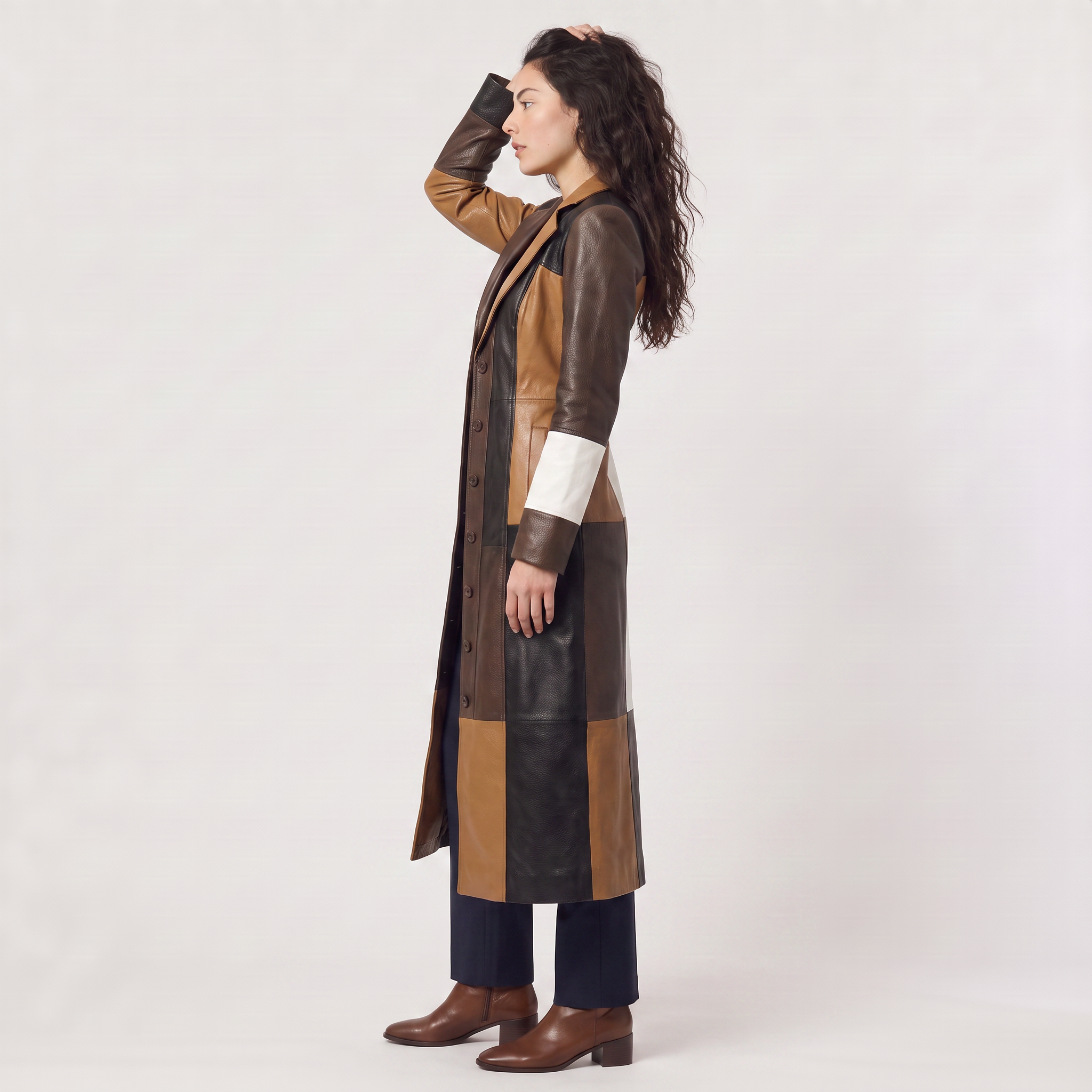 Women's trench coat featuring a stylish patchwork design in faux leather, showcasing a long structured silhouette in brown, black, and white colors. 3