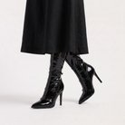 Black knee high boots featuring a sleek patent finish, inner zip closure, and stylish buckled straps, designed with elegant stiletto heels for women. 3