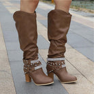 Black knee high boots featuring studded straps and a block heel, crafted from slouchy vegan leather for a stylish and comfortable fit for women. 0