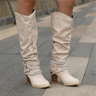 Black knee high boots featuring studded straps and a block heel, crafted from slouchy vegan leather for a stylish and comfortable fit for women. 2