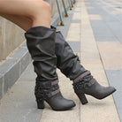 Black knee high boots featuring studded straps and a block heel, crafted from slouchy vegan leather for a stylish and comfortable fit for women. 6