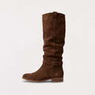 Knee high black boots for women featuring a slouch silhouette and buckled ankle tab, crafted from vegan materials with a low stacked heel. 8