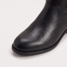 Knee high black riding boots for women with buckled ankle strap, made from faux leather and featuring a low stacked heel. 4