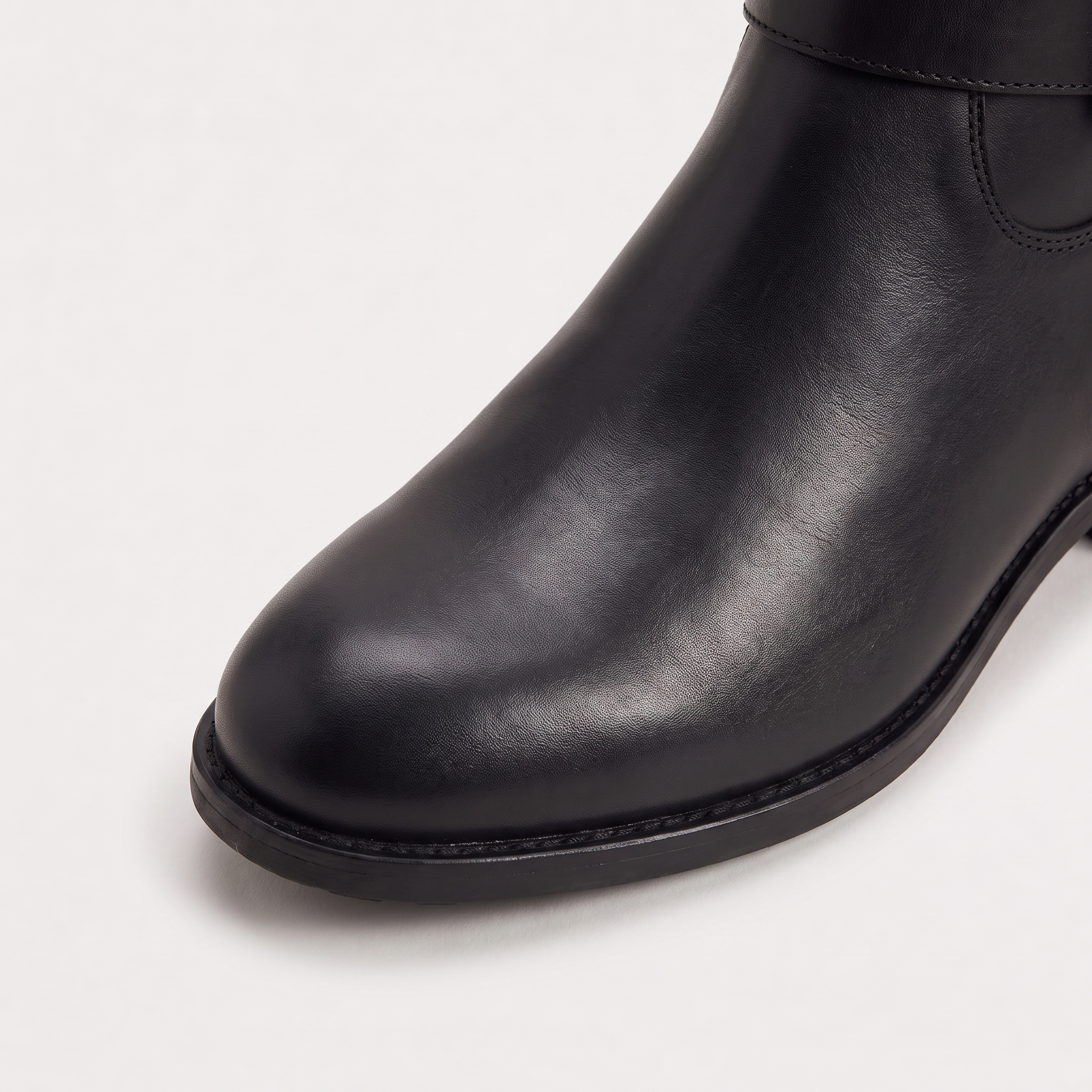 Knee high black riding boots for women with buckled ankle strap, made from faux leather and featuring a low stacked heel. 4