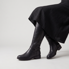 Knee high black riding boots for women with buckled ankle strap, made from faux leather and featuring a low stacked heel. 5