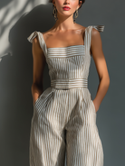 Linen blend jumpsuit featuring adjustable tie straps, square neckline, and wide-leg design in beige and white stripes. 2