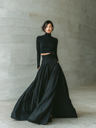 Women's outfit set featuring a fitted turtleneck cropped top and long skirt in black, designed with stretch knit material for a minimalist look. 2